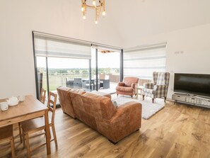 A spacious living area with a sofa, chairs, a dining table, and a TV.