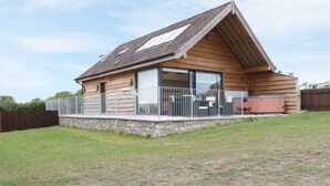A wooden cabin with a sloped roof, large windows, and a stone foundation. - Swan Lodge Castle Farm (Wedmore)