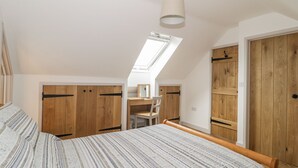 A bedroom with a sloped ceiling, a skylight, a bed with a striped bedspread, wooden wardrobes, and a desk with a chair. - Swan Lodge Castle Farm (Wedmore)