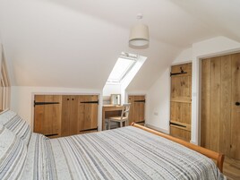 Un dormitorio con techo inclinado, tragaluces, cama con colcha a rayas, armarios de madera y un escritorio con silla.