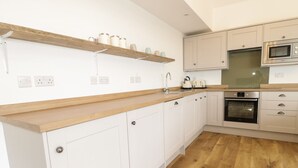 A modern kitchen with white cabinets, a wooden countertop, a built-in oven, a microwave, and a kettle. - Swan Lodge Castle Farm (Wedmore)