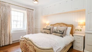 Un dormitorio con cama, mesitas de noche, una ventana con cortinas y una lámpara en el techo.