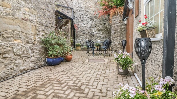 Un patio con paredes de piedra y suelo de ladrillo, zona de estar al aire libre con sillas de metal y plantas en macetas.
