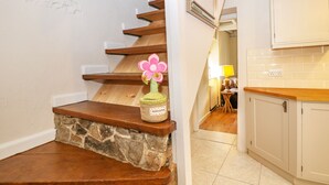 Una escalera con escalones de madera y base de piedra, que lleva a una zona de cocina con armarios blancos y salpicadero de azulejos.