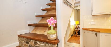 A staircase with wooden steps and a stone base, leading to a kitchen area with white cabinets and a tiled backsplash.