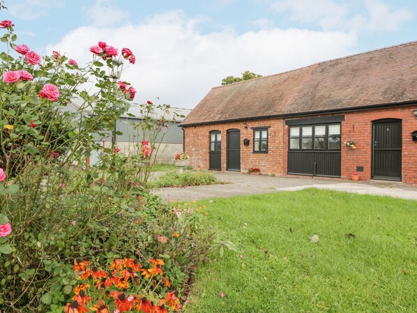 A brick building with a tiled roof, a front door, and a small garden area with flowers. - The Pheasant One (Usk)