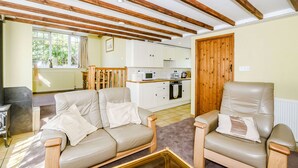 A living room with two beige sofas, a wooden coffee table, and a kitchen in the background. - Creenagh's Cottage (Minehead)