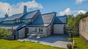 A house with a sloped roof, stone walls, and a small patio with outdoor furniture. - Creenagh's Cottage (Minehead)