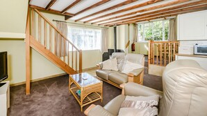 A cozy living room with a wooden staircase, a sofa, a glass coffee table, and a kitchen area with a microwave. - Creenagh's Cottage (Minehead)
