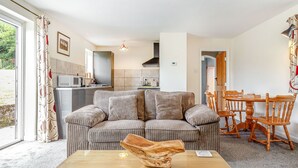 A living room with a glass-top coffee table, striped sofa, wooden dining table, and chairs. - Foxlair Cottage (Minehead)