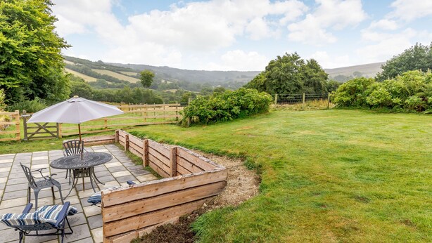 A patio with outdoor furniture, a wooden fence, and a view of a grassy field and hills. - Foxlair Cottage (Minehead)