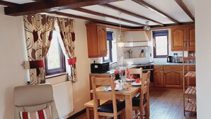 Une cuisine chaleureuse avec des meubles en bois, une table à manger dressée pour quatre personnes et une chaise agrémentée d’un coussin à rayures.