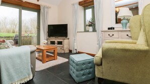 Un salon comprenant un téléviseur, un canapé, un fauteuil, une table basse et un petit pouf.
