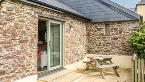 Une maison en pierre avec un toit en tuiles, une porte-fenêtre coulissante et une table de pique-nique en bois.