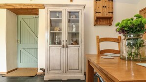 Un coin repas comprenant une table en bois, un meuble avec des portes en verre et une chaise en bois.