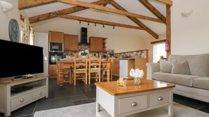 A spacious living room with a flat-screen TV, wooden dining table, and a sofa. - Hawthorn Cottage (Truro)