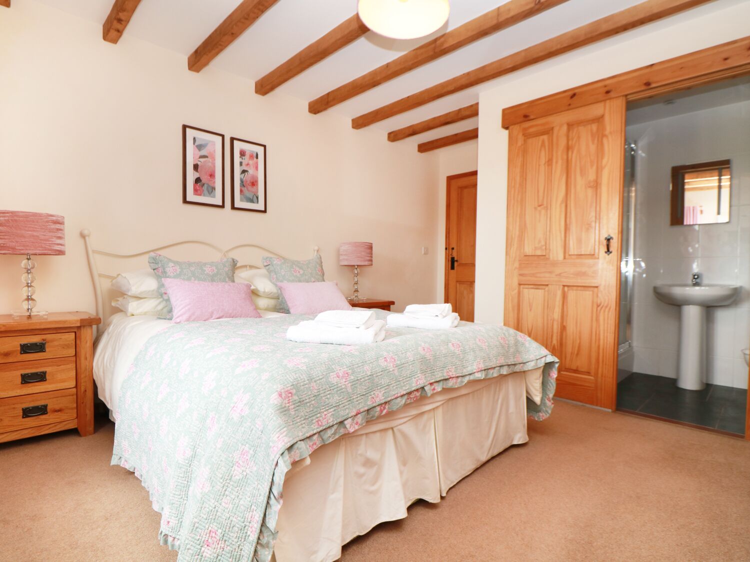 Une chambre à coucher comprenant un lit, des tables de chevet, une armoire en bois et une salle de bain avec un lavabo.