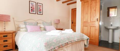 Une chambre à coucher comprenant un lit, des tables de chevet, une armoire en bois et une salle de bain avec un lavabo.