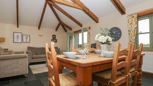 A dining area with a wooden table set for four, surrounded by wooden chairs with cushions. - Hawthorn Cottage (Truro)