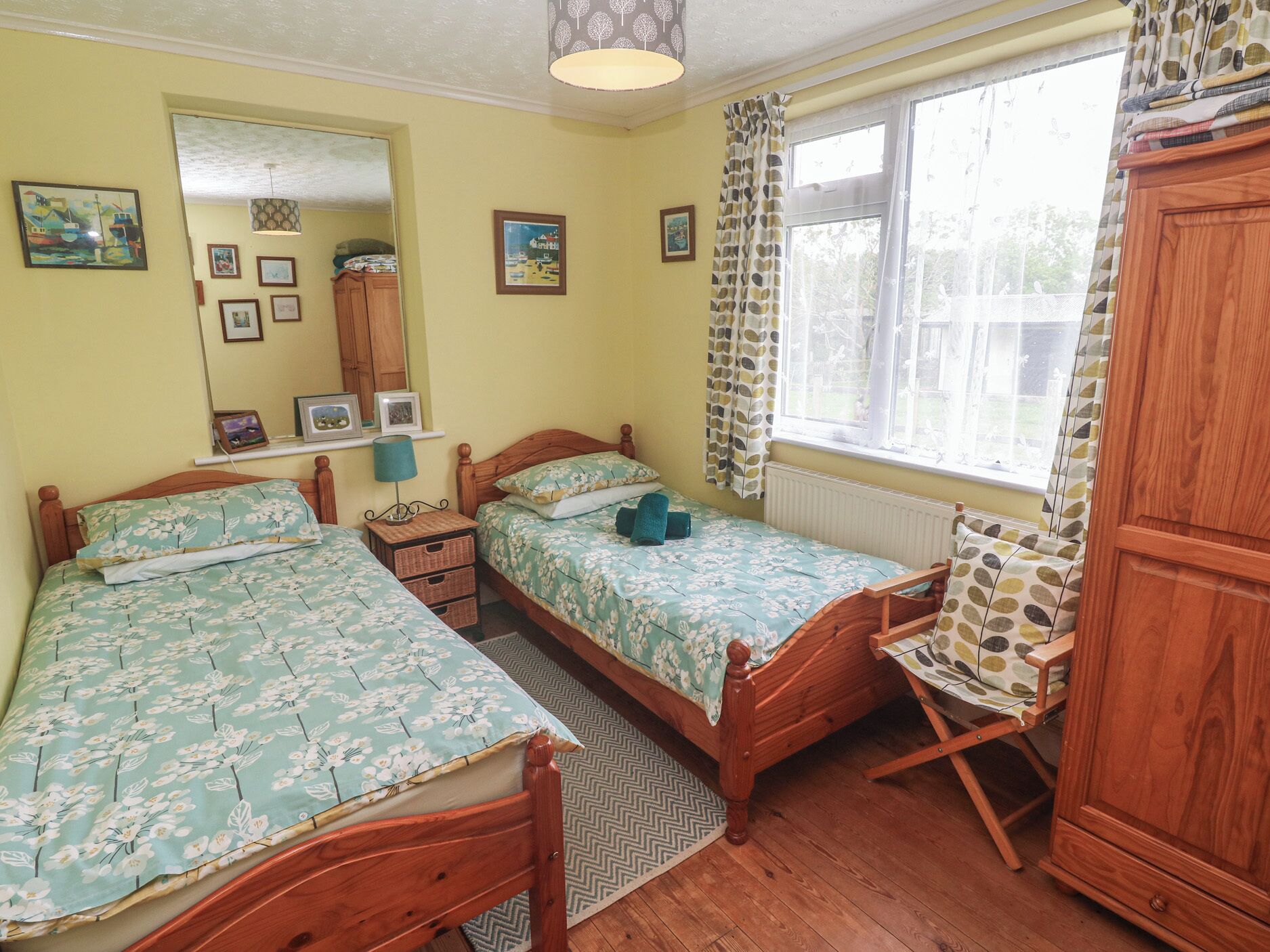 A bedroom with two wooden beds, a wooden wardrobe, a mirror, and a window with curtains.