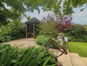 A gazebo with a sloped roof, surrounded by a gravel path and lush greenery. - Woolly Welcome (Penzance)