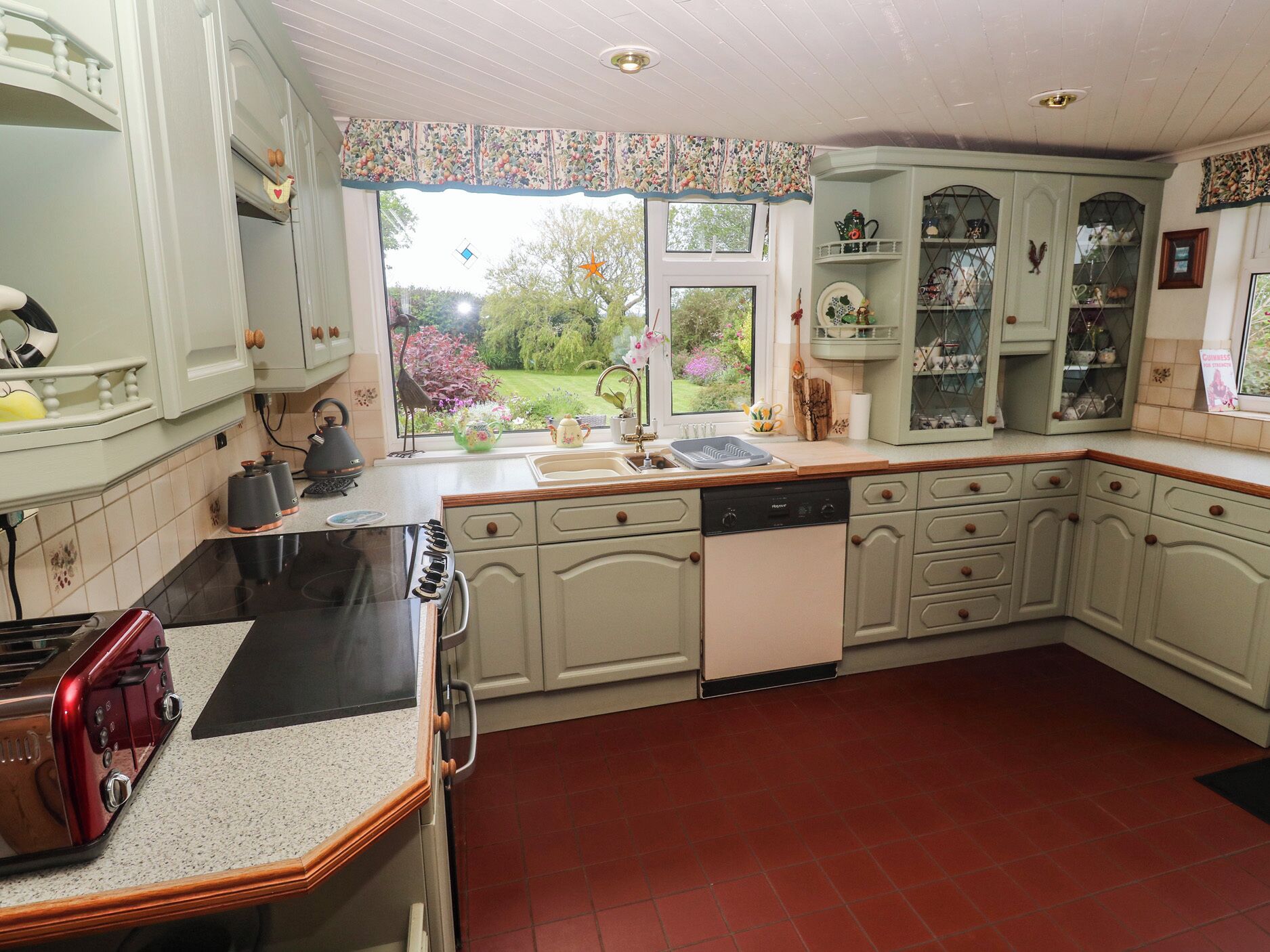 A kitchen with a stove, oven, and sink, with a window overlooking a garden.