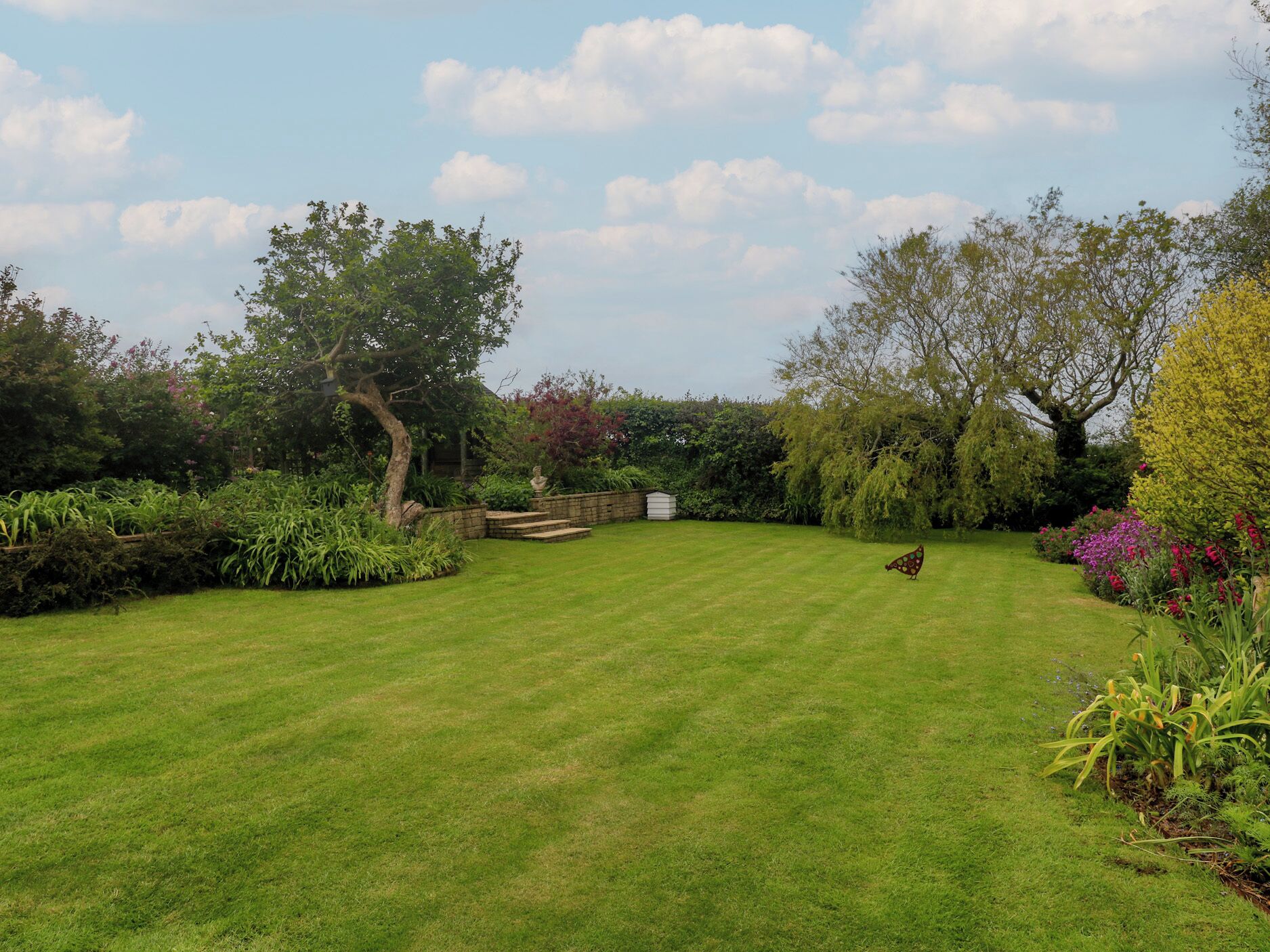 Un jardin bien entretenu, avec une pelouse, des marches en pierre et divers arbustes et arbres.
