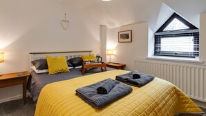A bedroom with a bed, a nightstand, a lamp, a window with blinds, and a radiator. - 2 Ysgoldy (Bangor)