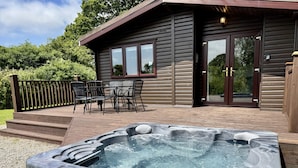 Een hottub voor een houten chalet met terras en tuinmeubilair.