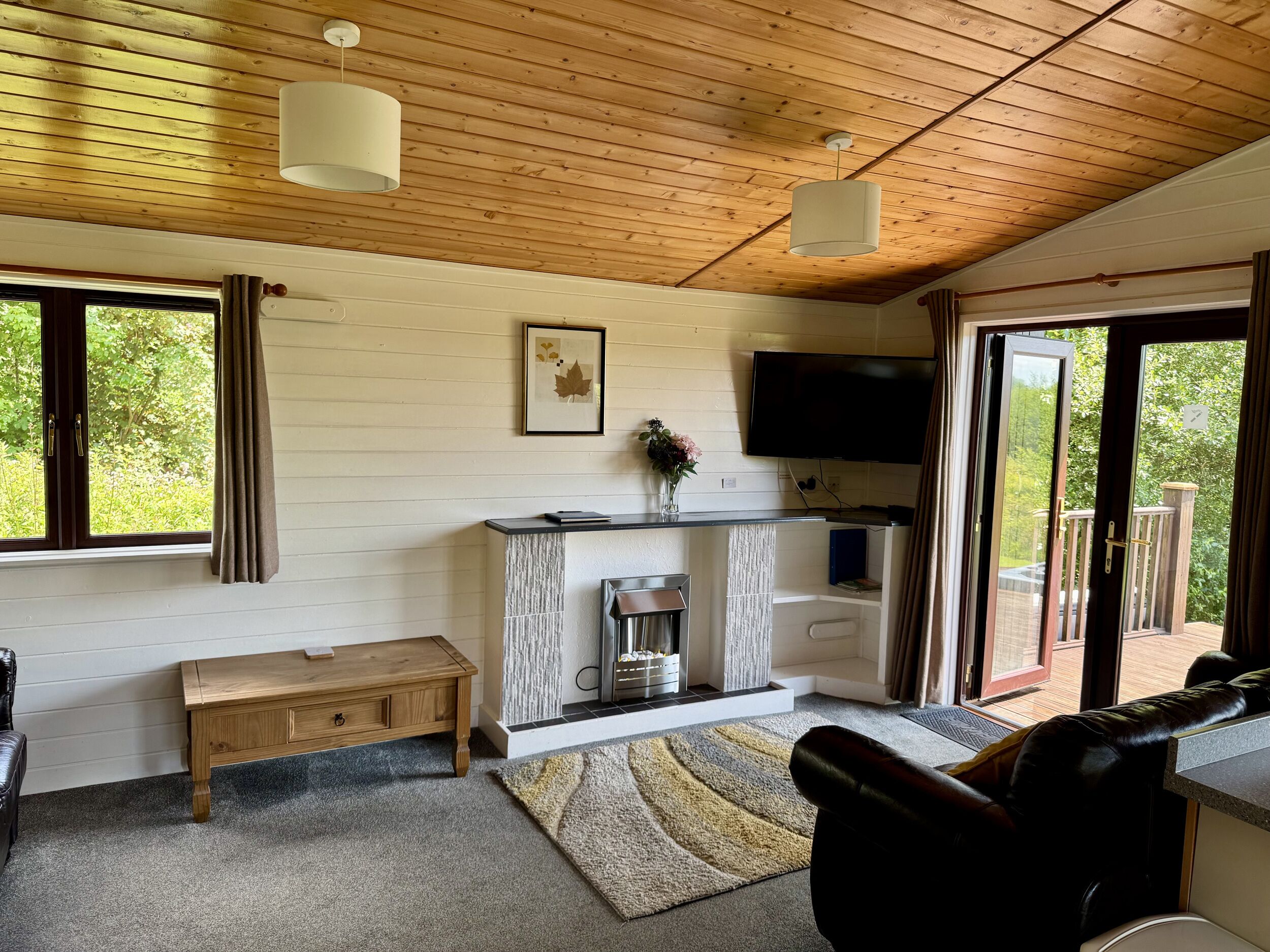 A cozy living room with a fireplace, a flat-screen TV, and a large window offering a view of the outdoors.