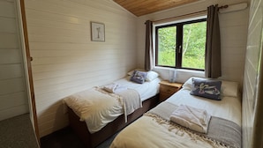 Een slaapkamer met twee bedden, een houten plafond, een raam met gordijnen en een nachtkastje met een lamp.