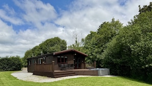 Een houten chalet met een veranda en buitenmeubilair, omgeven door weelderig groen en bomen.