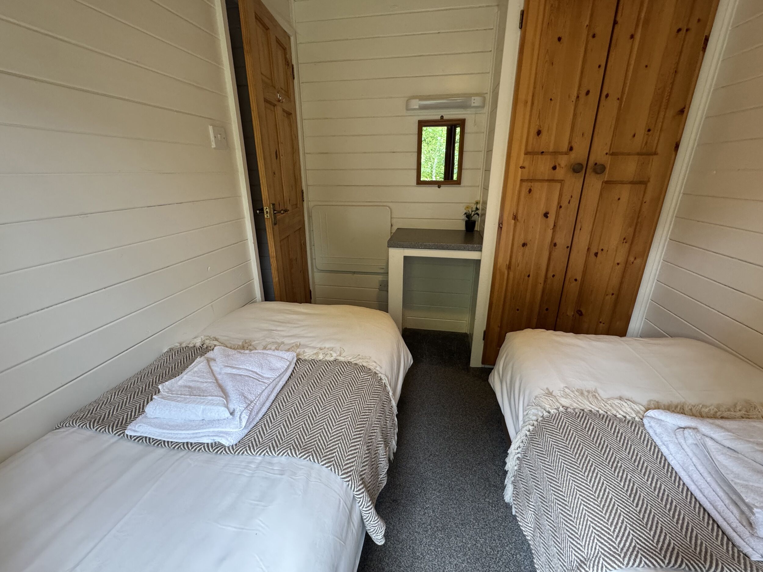 A small, compact room with two single beds, a small desk, and a window.
