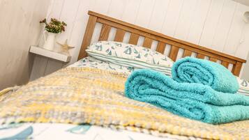 A neatly made bed with a patterned bedspread, a rolled blue towel, and a starfish decoration on a bedside table.