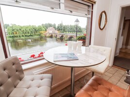 A room with a table and chairs near a window overlooking a river and bridge.