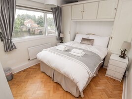 A bedroom with a bed, a nightstand, a lamp, a window with curtains, a radiator, and a view of a bridge and buildings outside.