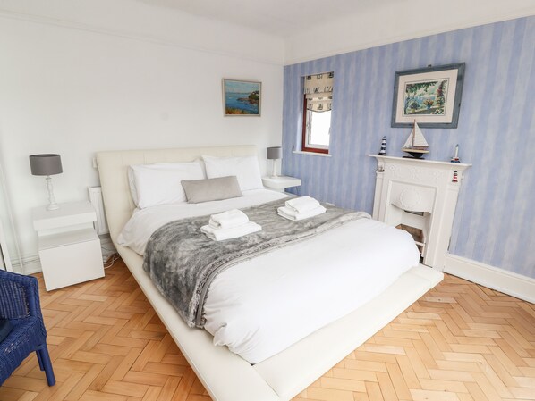 A bedroom with a bed, nightstands, a dresser, a blue chair, a fireplace, and two framed pictures on the wall. - Dee Heights Penthouse (Chester)