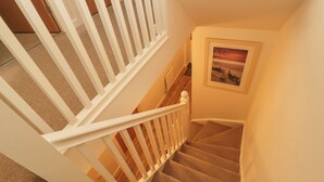 Un escalier avec des rampes blanches et des marches recouvertes de moquette, menant à un palier.
