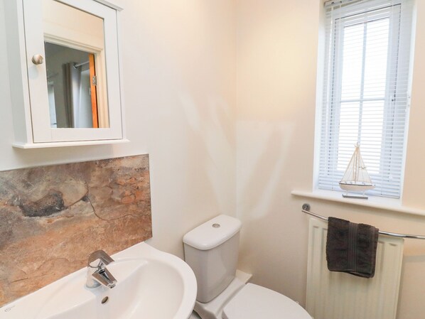 Een badkamer met een achterwand van steen, een witte wastafel, een toilet en een raam met luxaflex.