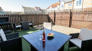 Une terrasse avec des meubles d’extérieur, une table avec une bouteille et un verre, et un barbecue.