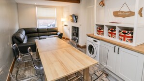Ett kompakt bostadsutrymme med ett matbord i trä, en svart lädersoffa, en tvättmaskin och ett vitt skåp med förvaringslådor.