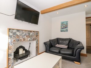 A living room with a black leather sofa, a white table, a fireplace with a patterned mantel, a mounted TV, and a painting on the wall. - 11A Church Street (Whitby)