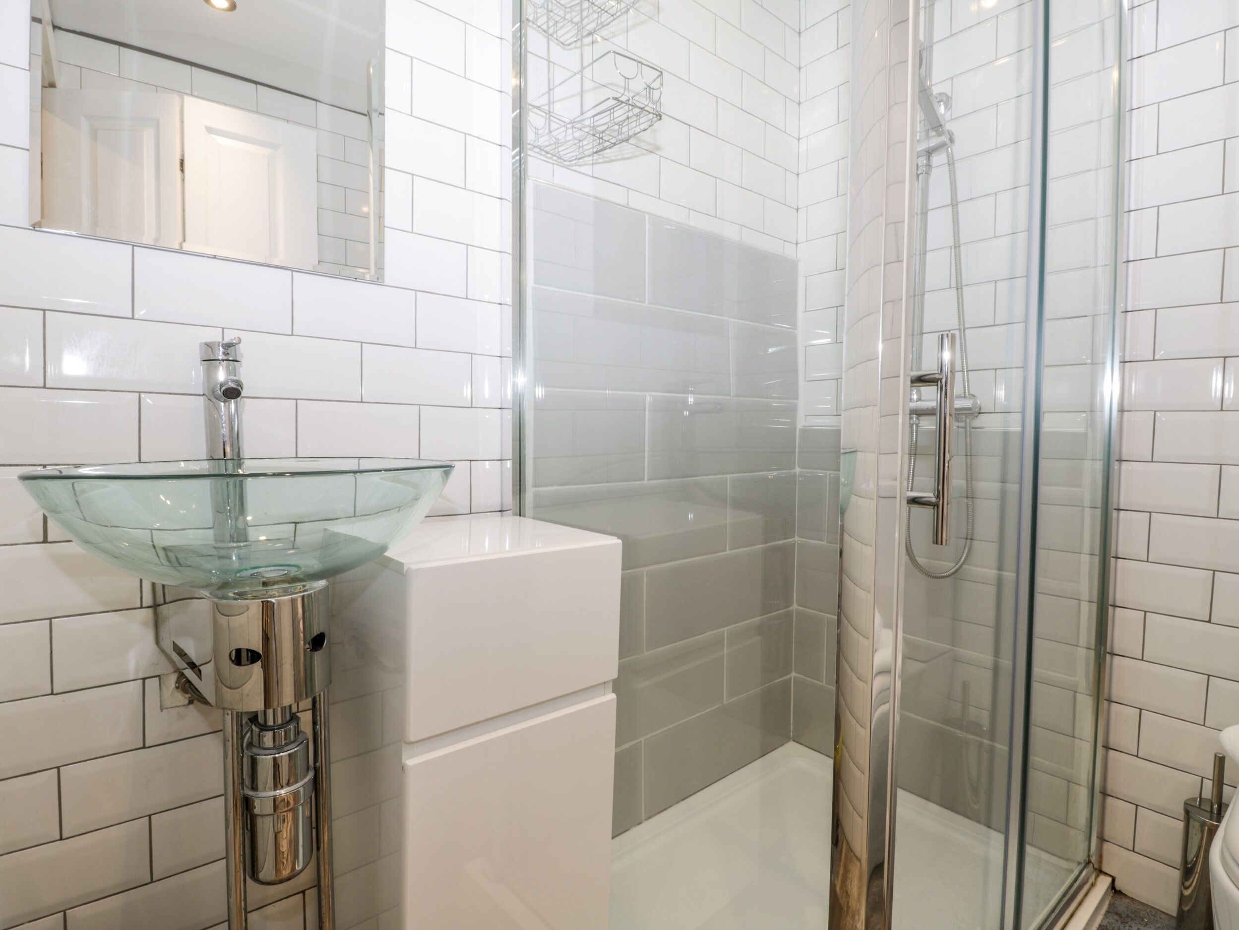 A modern bathroom with a glass sink, white tiles, and a glass-enclosed shower.