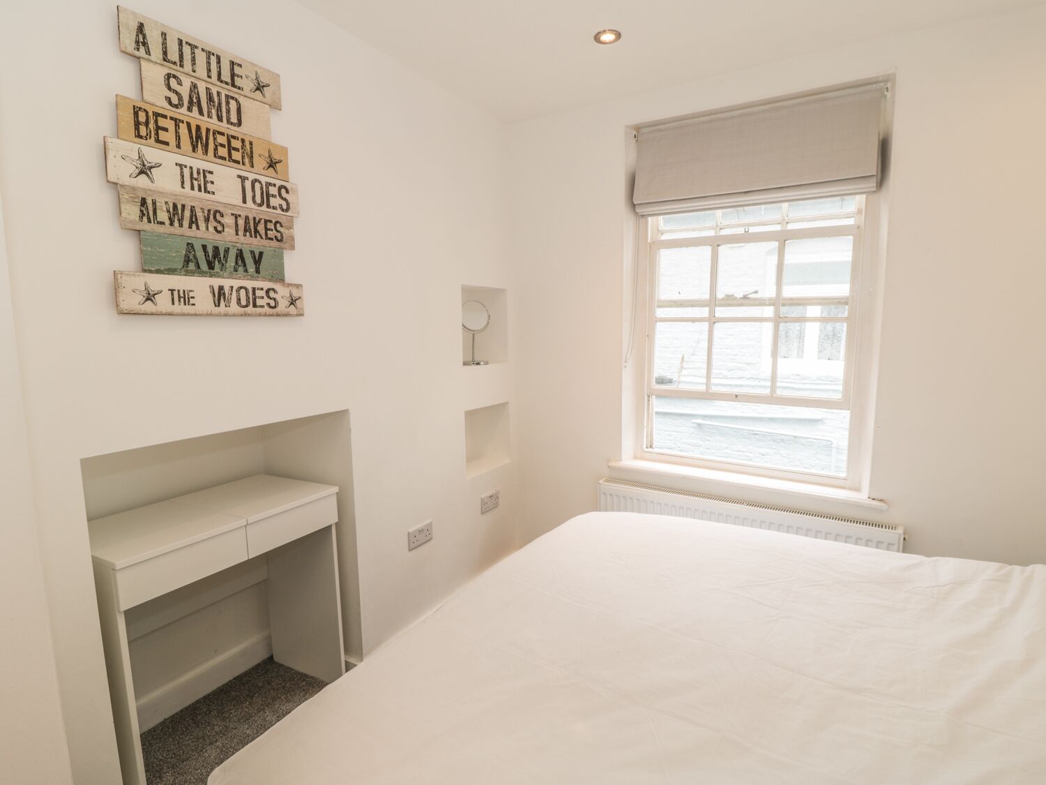 A bedroom with a bed, a desk, and a window with a view of the sea.