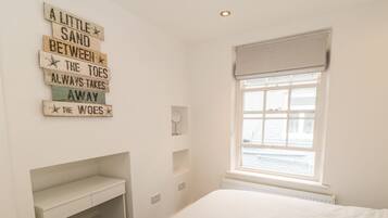 A bedroom with a bed, a desk, and a window with a view of the sea.