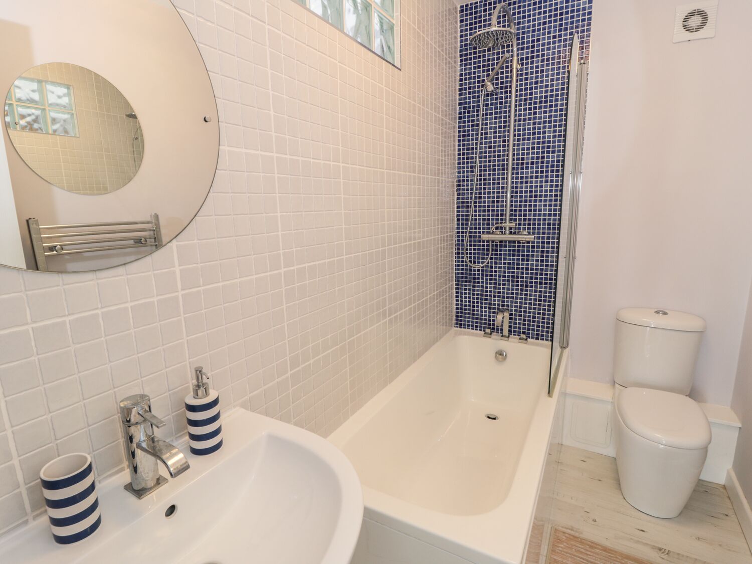 A bathroom with a white sink, a bathtub, a shower with blue tiles, and a toilet.