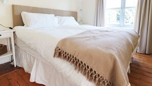 Une chambre à coucher avec un grand lit, une table de chevet, une lampe et une fenêtre avec des rideaux.