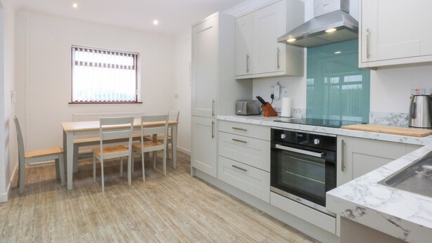 Une cuisine moderne avec des meubles blancs, un four encastré et un coin repas comprenant une table et des chaises.