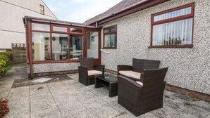 Une terrasse dotée de meubles en osier et d’une porte vitrée donnant sur une pièce.