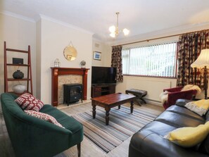 A living room with a fireplace, a sofa, a television, and a patterned rug. - Eryl (Pwllheli)
